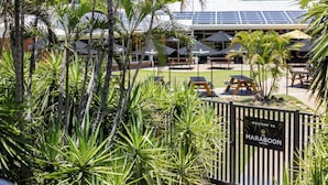 A tropical outdoor seating area with palm trees, a sign reading "Welcome to Maraboon Tavern," and solar panels on the building.