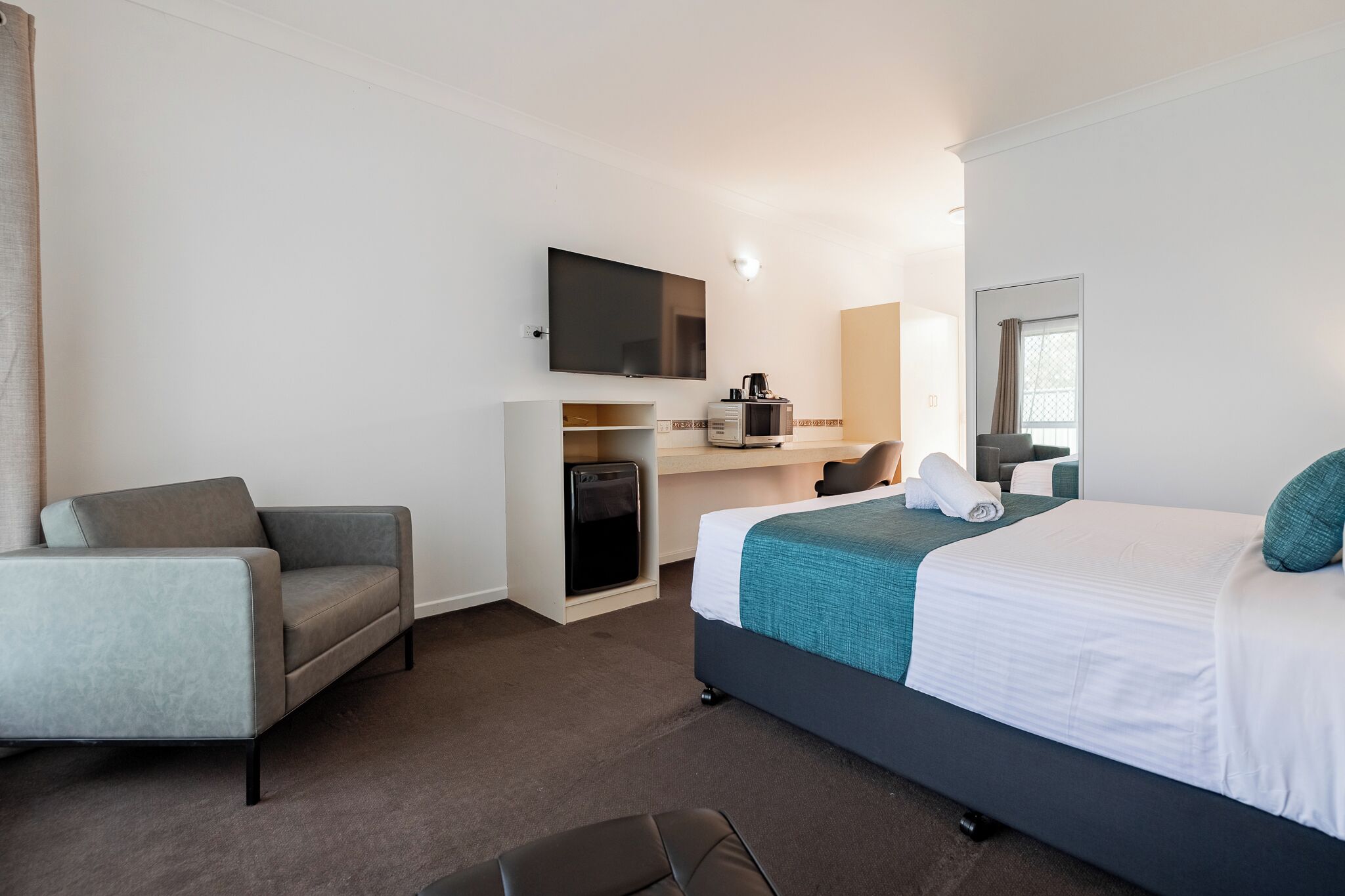 A hotel room with a bed, a sofa, a desk, a TV, and a microwave.
