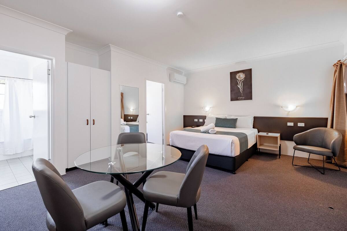 A hotel room with a bed, bedside tables, a glass table with chairs, and a large mirror.