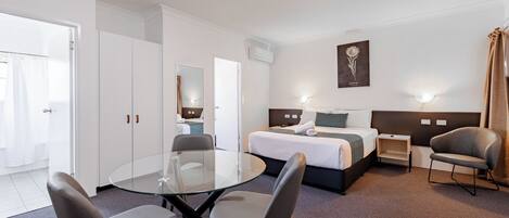 A hotel room with a bed, bedside tables, a glass table with chairs, and a large mirror.