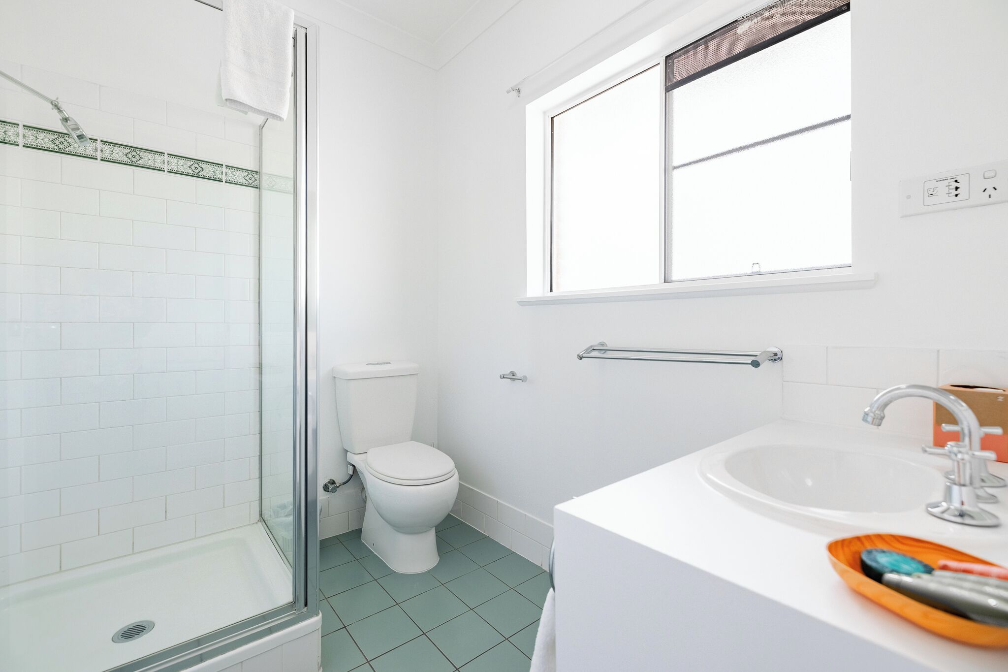 A bathroom with a glass shower enclosure, a toilet, a sink with a mirror, and a window.