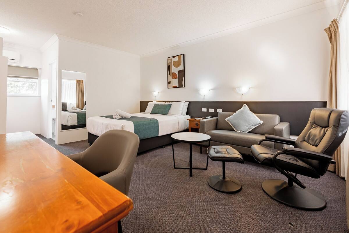 A hotel room with a bed, a sofa, a recliner, a small table, and a wooden desk.