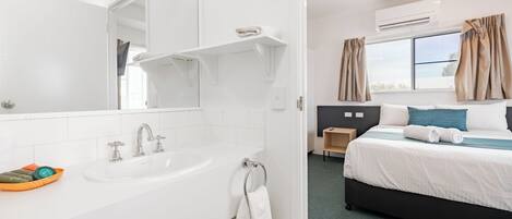 Une chambre d’hôtel avec un lavabo blanc, un miroir et un lit avec un oreiller bleu.