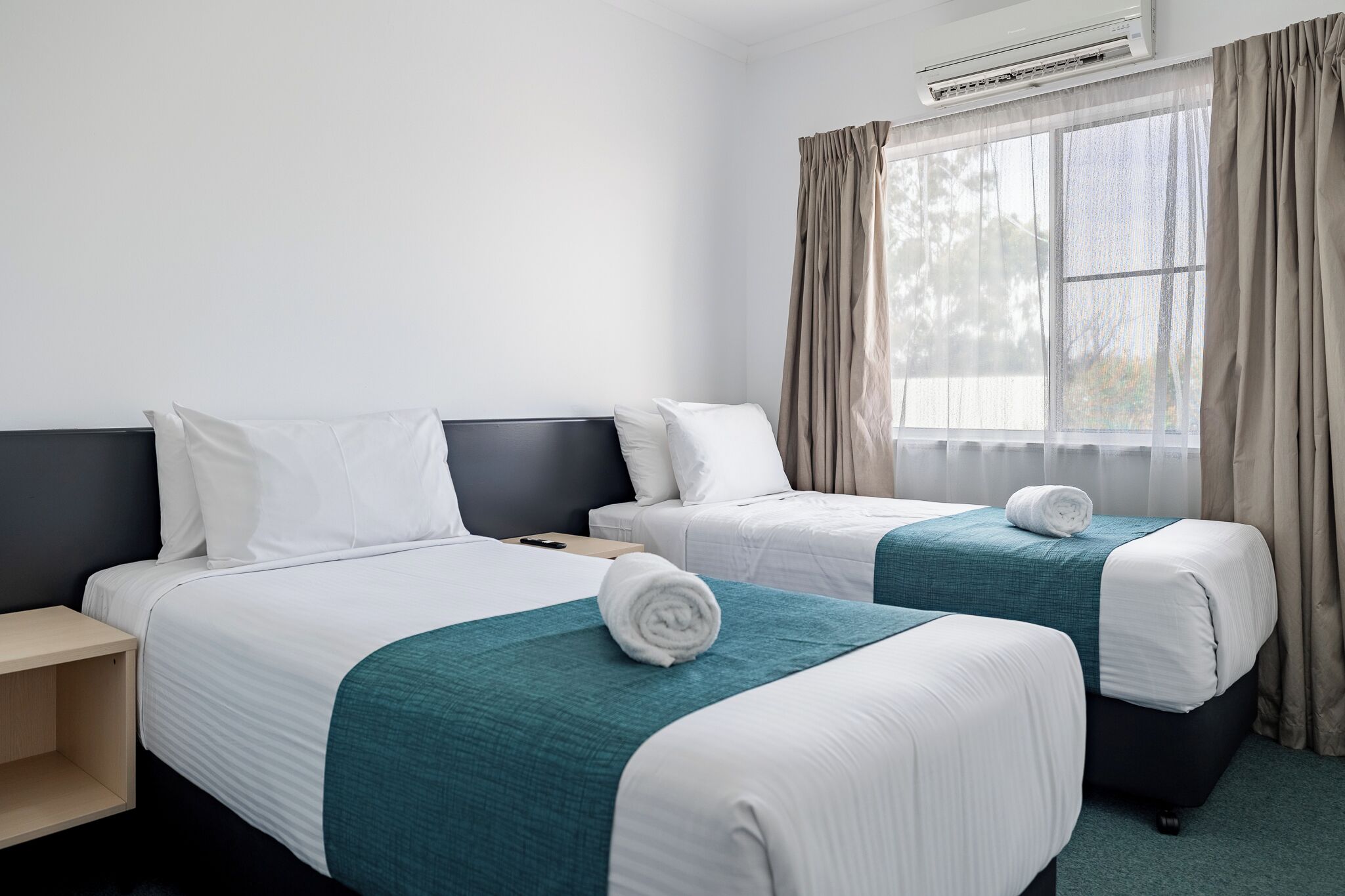 A hotel room with two beds, a nightstand, and a window with curtains.