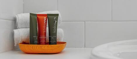 A bathroom with a white tiled wall, a white towel, and three bath products in a wooden bowl.