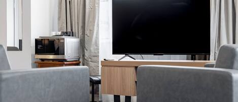 Une chambre d’hôtel équipée d’un téléviseur à écran plat posé sur un meuble en bois, d’un four à micro-ondes, d’un bureau en bois et de chaises grises recouvertes de tissu.
