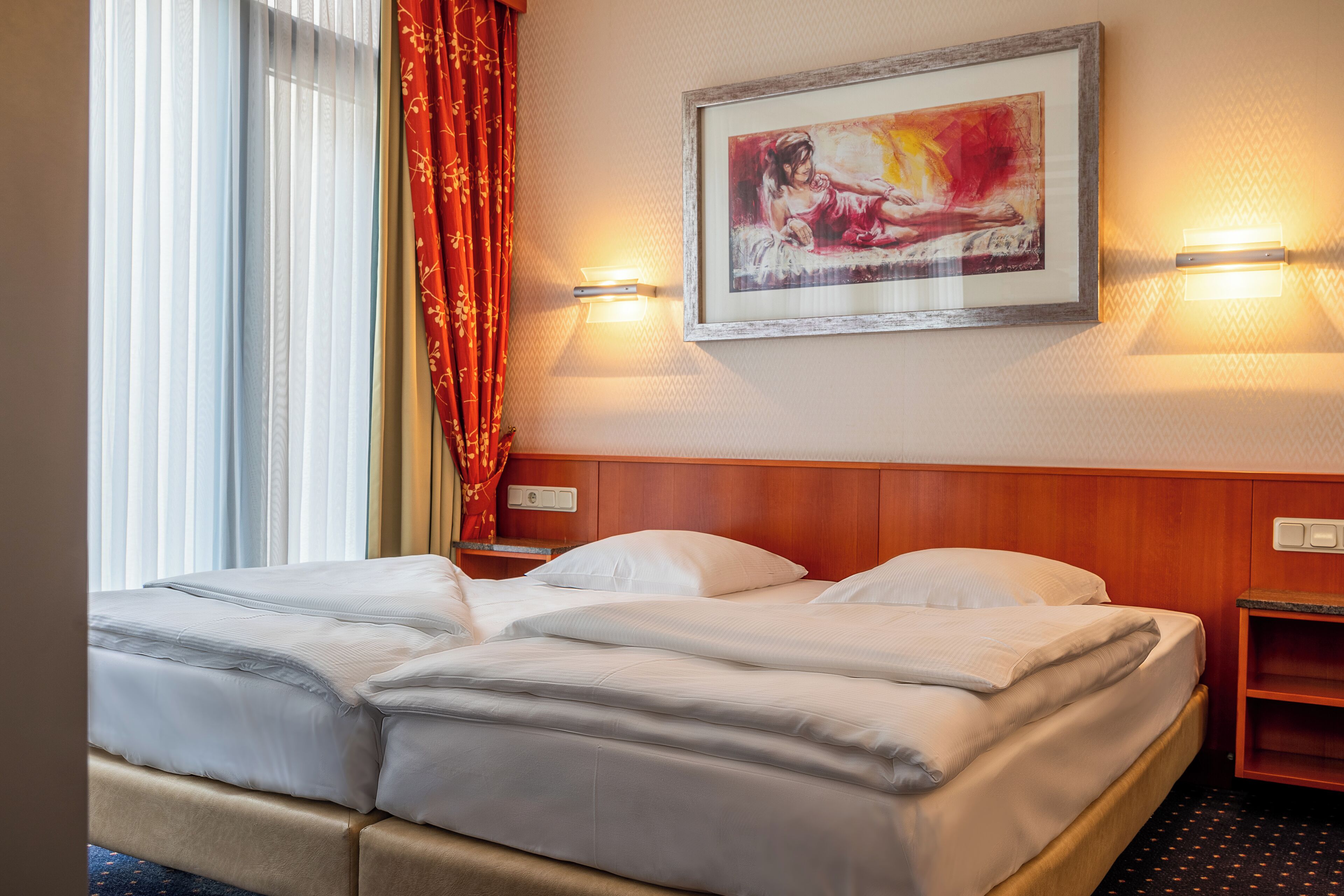 Une chambre d’hôtel avec un lit double, deux tables de chevet, une petite table, un tableau encadré et deux lampes fixées au mur.