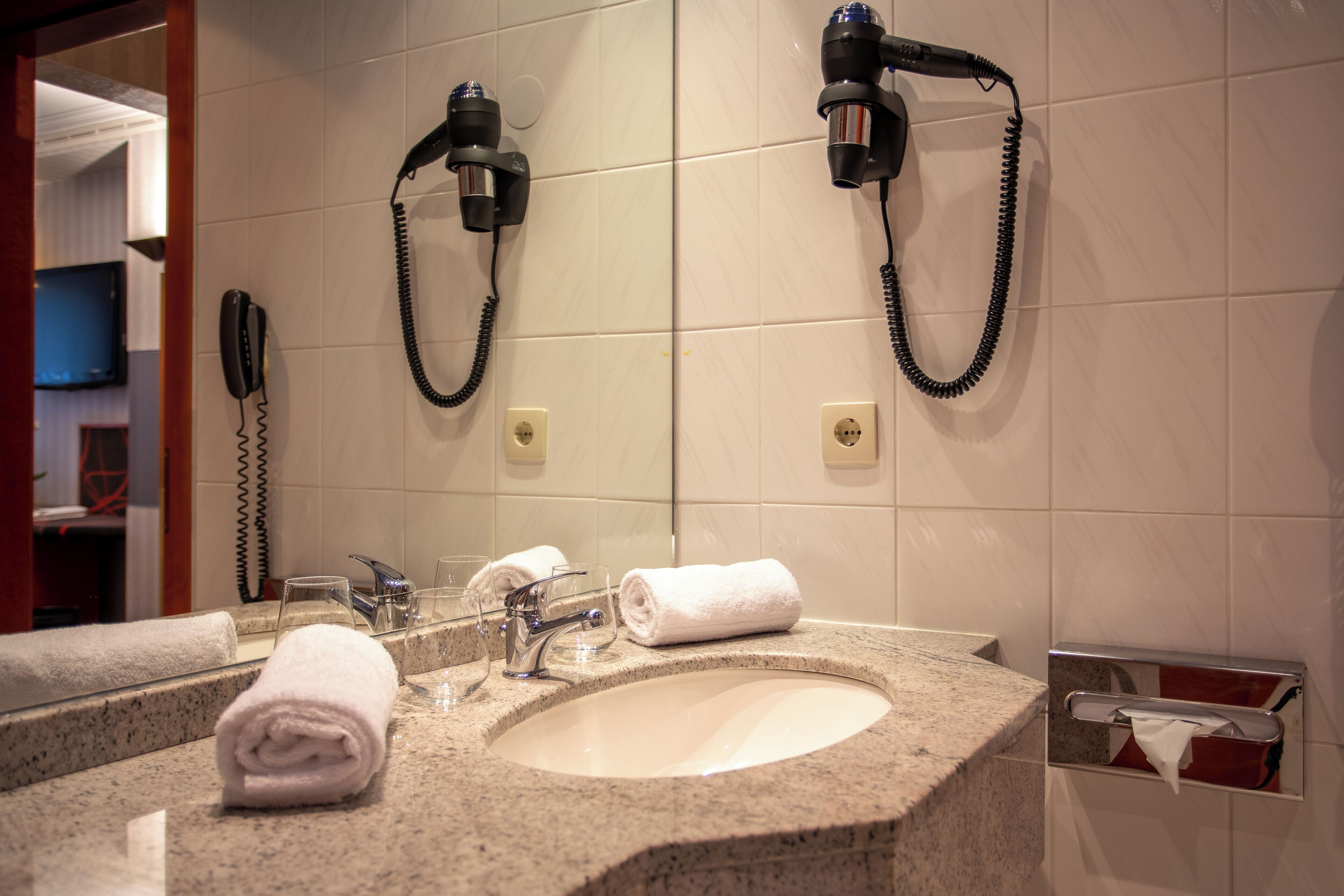 A bathroom with a sink, two hair dryers, a telephone, and a towel rack.