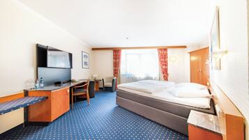 Ein Hotelzimmer mit Bett, Schreibtisch, Stuhl, Fernseher und einem Fenster mit Vorhängen.