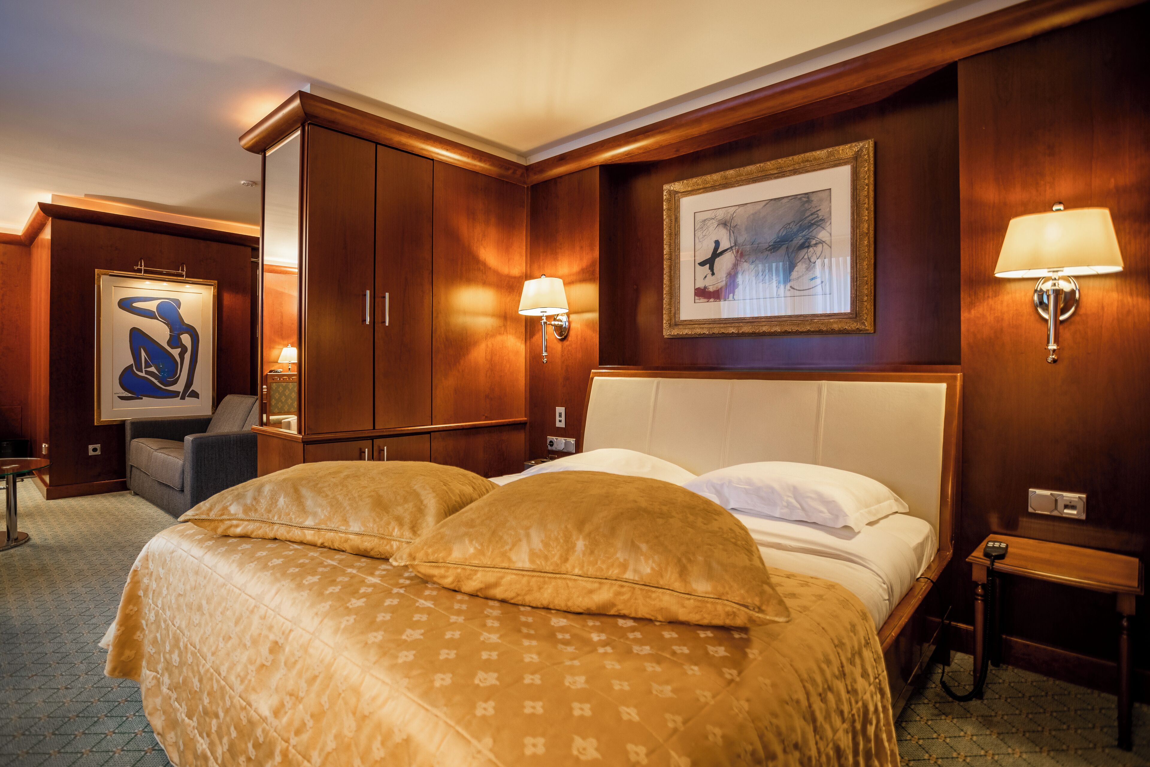 A hotel room with a large bed, a desk, a chair, and a painting on the wall.