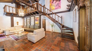 A spacious living area with a staircase, a chandelier, and a large painting on the wall.