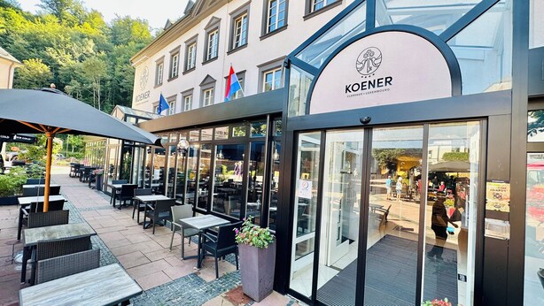 An outdoor seating area with tables and chairs, a glass storefront, and a flag.