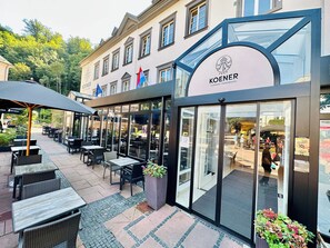 An outdoor seating area with tables and chairs, a glass storefront, and a flag.