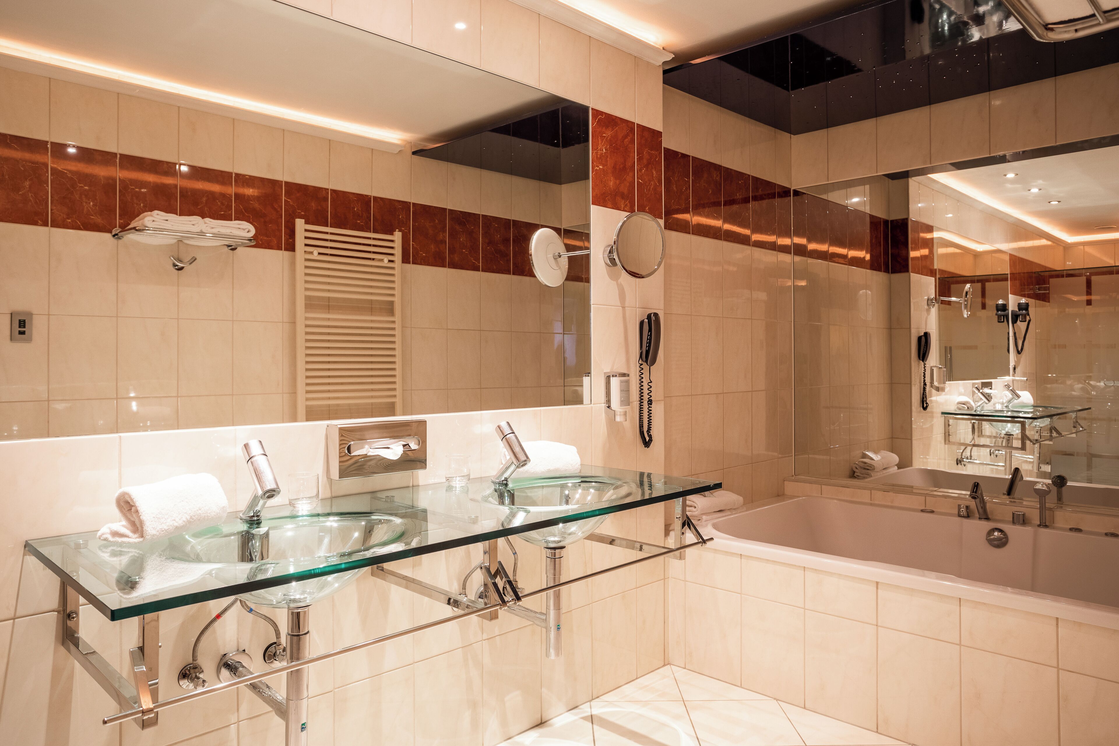 Un baño moderno con un lavabo de vidrio, un espejo grande y una bañera.