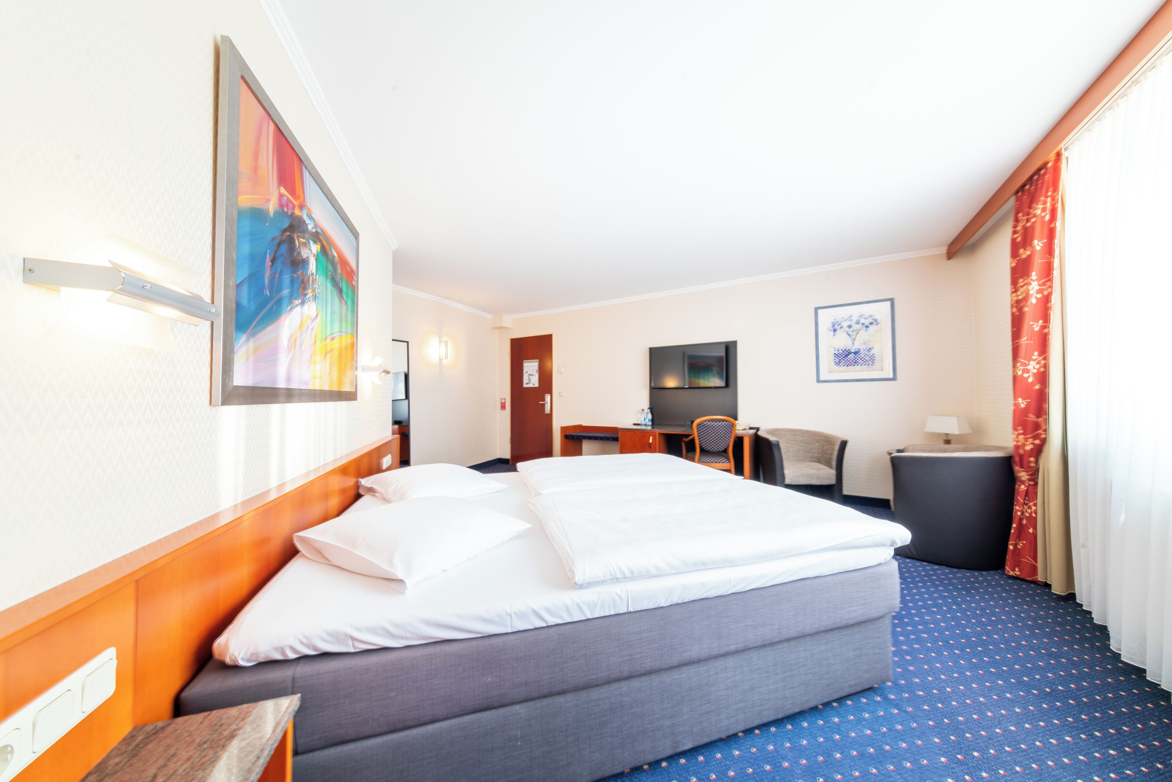 Una habitación de hotel con una cama grande, un escritorio, una silla y un televisor en la pared.