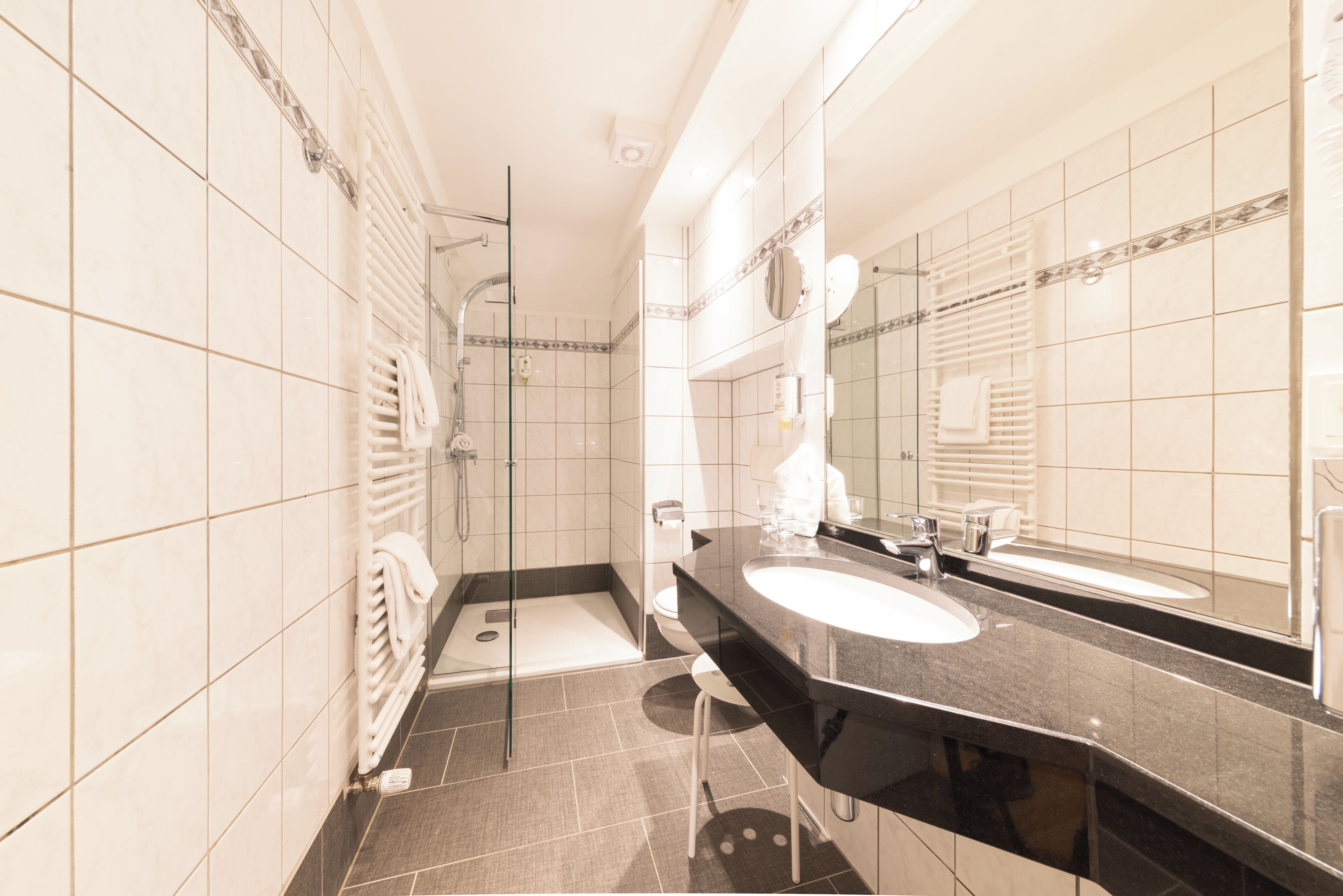 A modern bathroom with a black countertop, two sinks, a glass shower enclosure, and a large mirror.