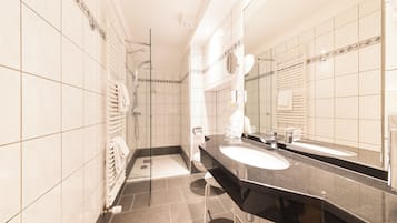 A modern bathroom with a black countertop, two sinks, a glass shower enclosure, and a large mirror.
