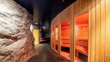 Un pasillo con paredes y bancos de madera, que conduce a una zona de sauna con bancos rojos y una pared de piedra en un lateral.