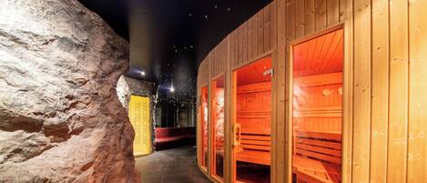 A hallway with wooden walls and benches, leading to a sauna area with red benches and a stone wall on one side.