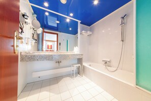 A modern bathroom with a large mirror, a granite countertop, a built-in toilet, and a separate shower area.