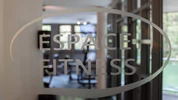 En glasdør med ordene "ESPACE FITNESS" indgraveret, der afspejler et indre rum med træningsudstyr.
