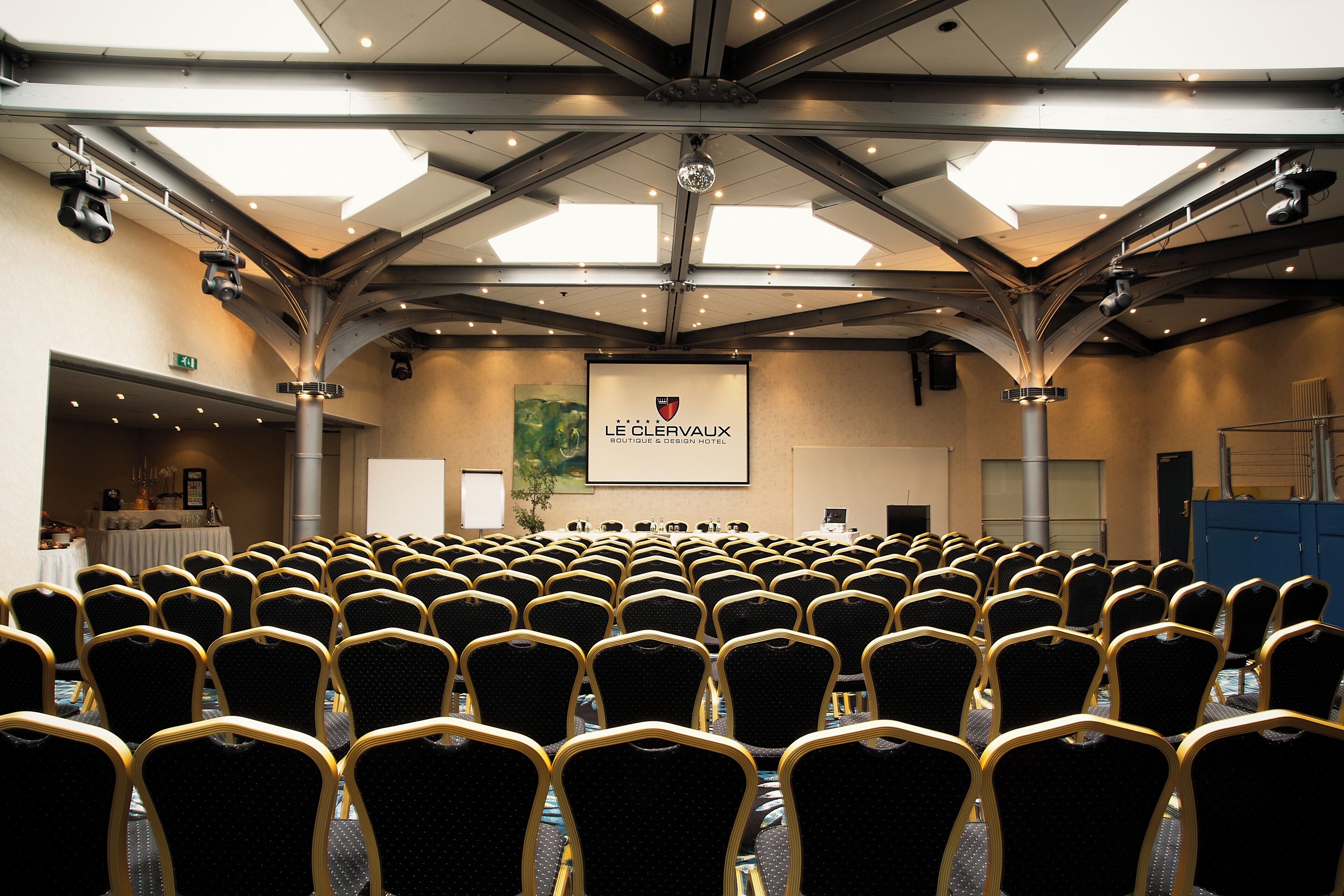 Ein Konferenzraum mit Reihen von Stühlen, einer Präsentationsleinwand und einer Kandelaber.