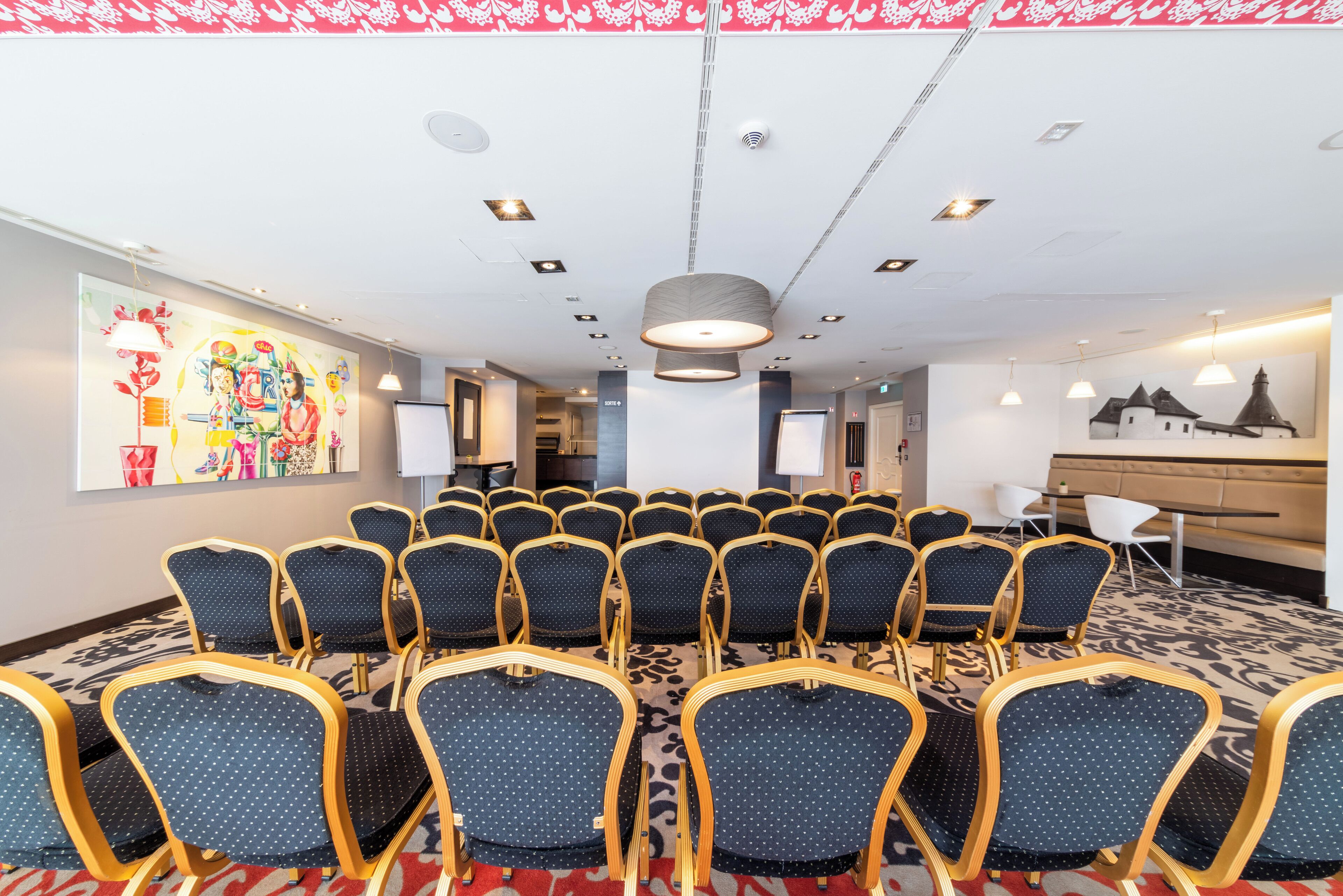 Un salón de conferencias con filas de sillas, un cuadro grande en la pared y una alfombra estampada.