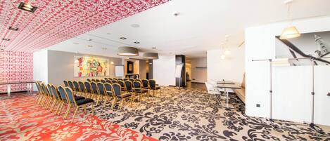 Un salón de conferencias con alfombra estampada, filas de sillas, una pizarra y un ventanal grande.