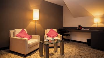 Une chambre d’hôtel avec deux fauteuils, une table basse en verre, un minibar et deux lampes fixées au mur.