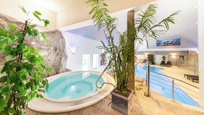 An indoor swimming pool with a hot tub, surrounded by plants and a rocky wall.