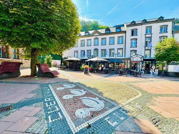 A cobblestone plaza with outdoor seating, a tree, and a building with multiple windows and a sign for Hotel Konec.