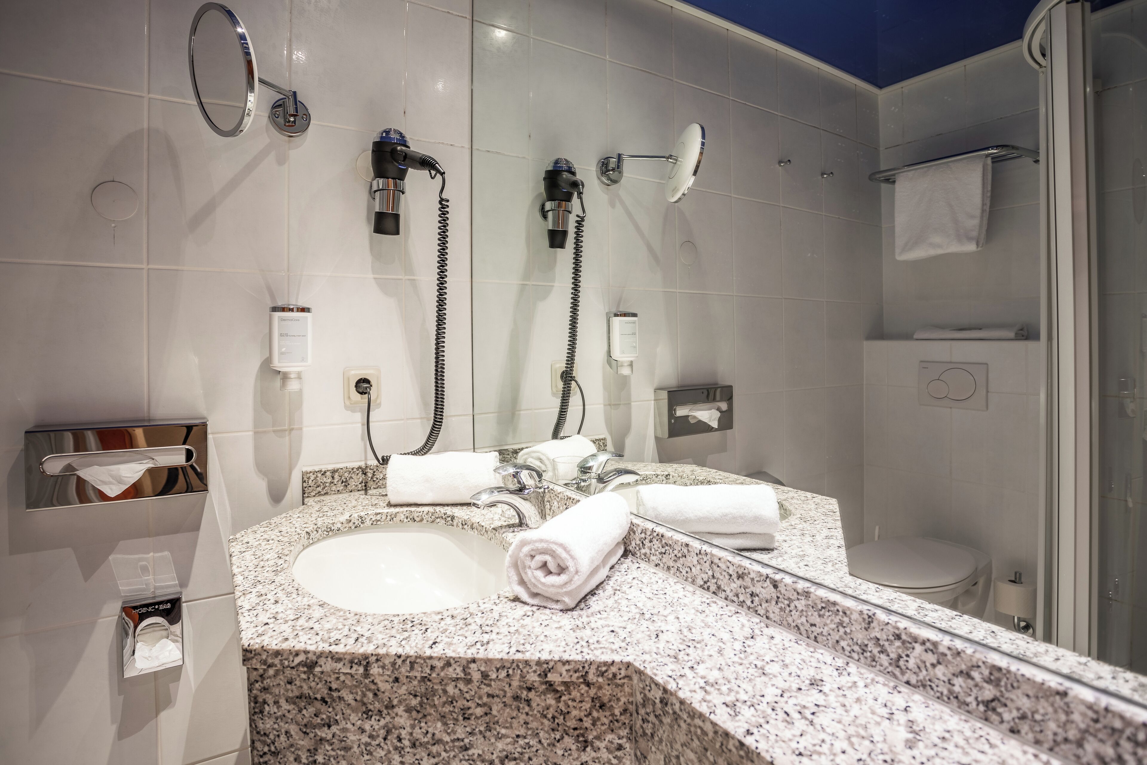 Un baño moderno con lavamanos de granito, un espejo grande, cabina de ducha de vidrio y un inodoro.
