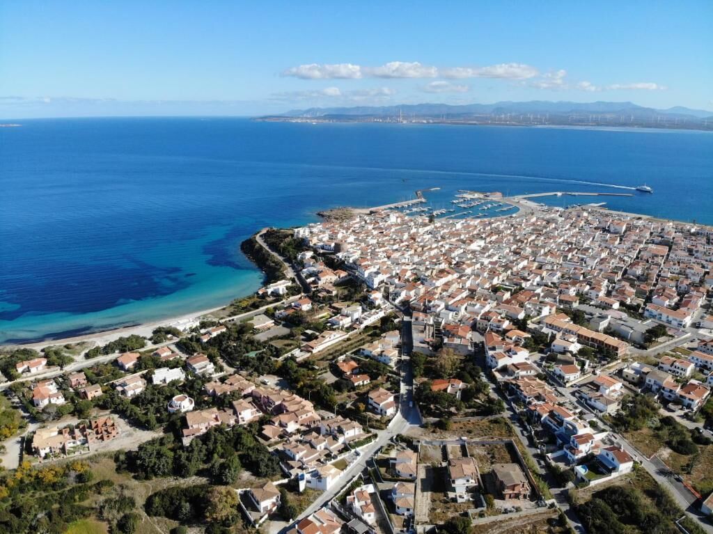 An aerial view of a coastal town with a marina, dense residential area, and clear blue sea.