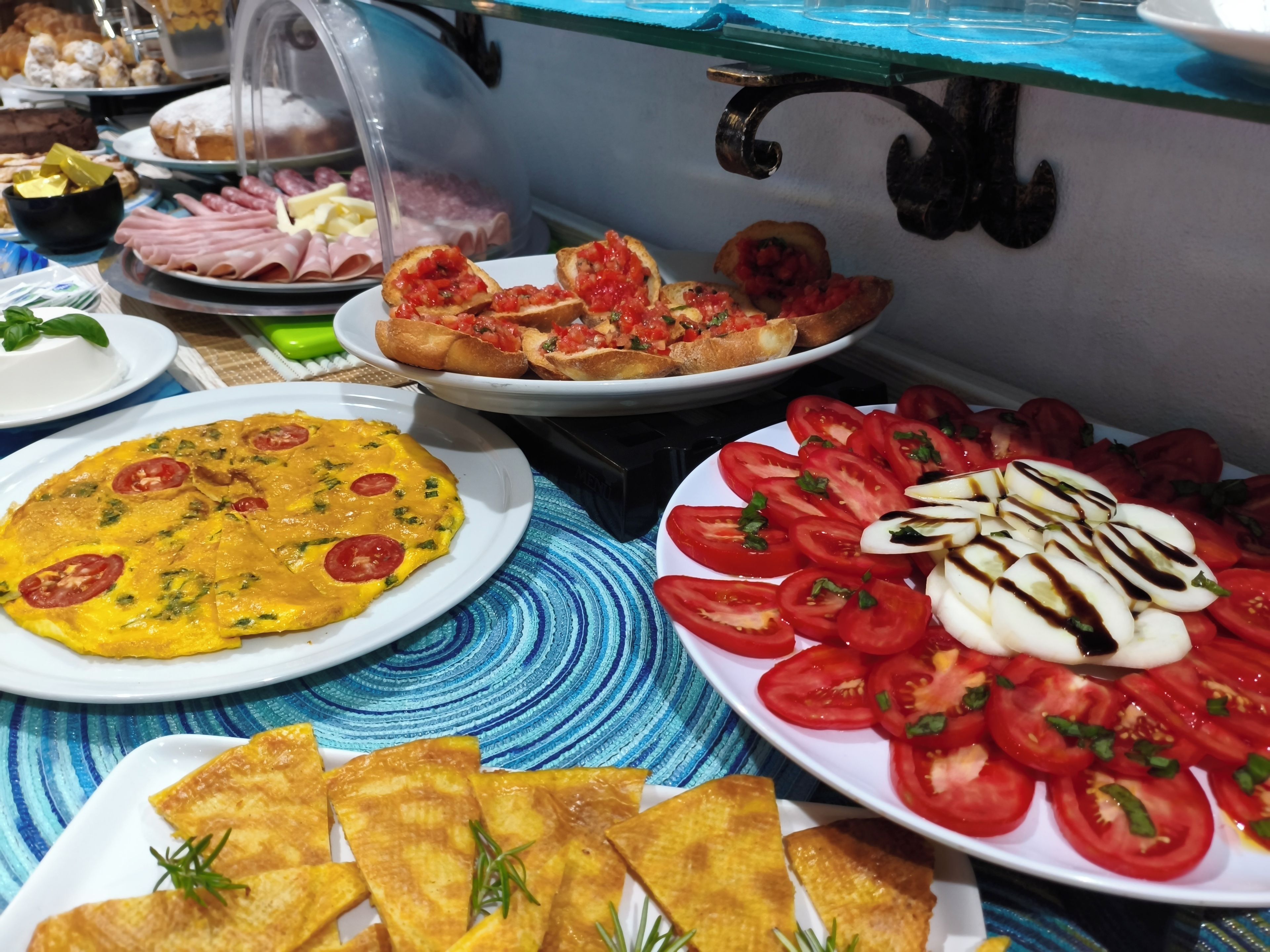 Un bufé con diversos platos, incluyendo una tortilla, ensalada de tomate y pan.