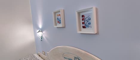 Ein Schlafzimmer mit einem Bett, einem Nachttisch und zwei gerahmten Kunstwerken an der Wand.