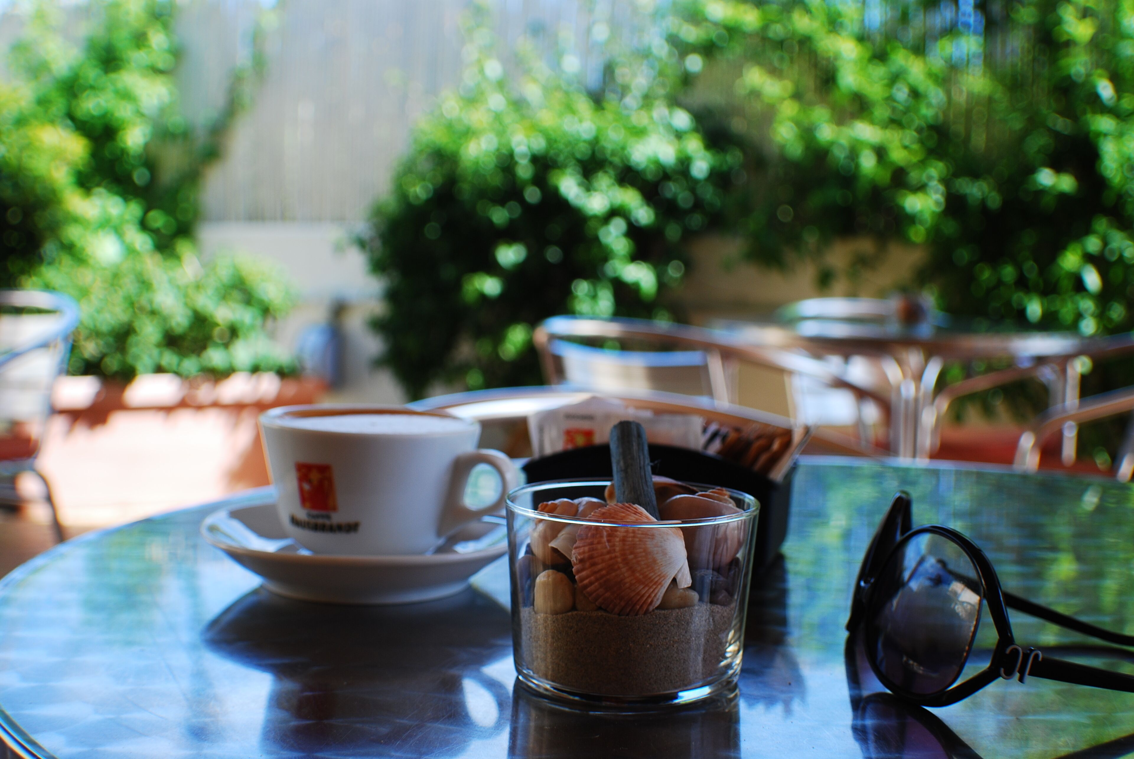 Una mesa de vidrio con una taza de café, un vaso con hielo y un par de gafas de sol.