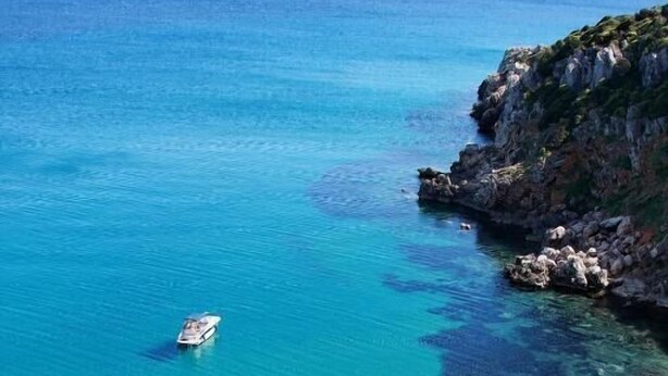 Una zona costera con agua turquesa cristalina, costas rocosas y un barco a lo lejos.