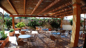 Un patio al aire libre con varias mesas y sillas, cubierto por una pérgola de madera.