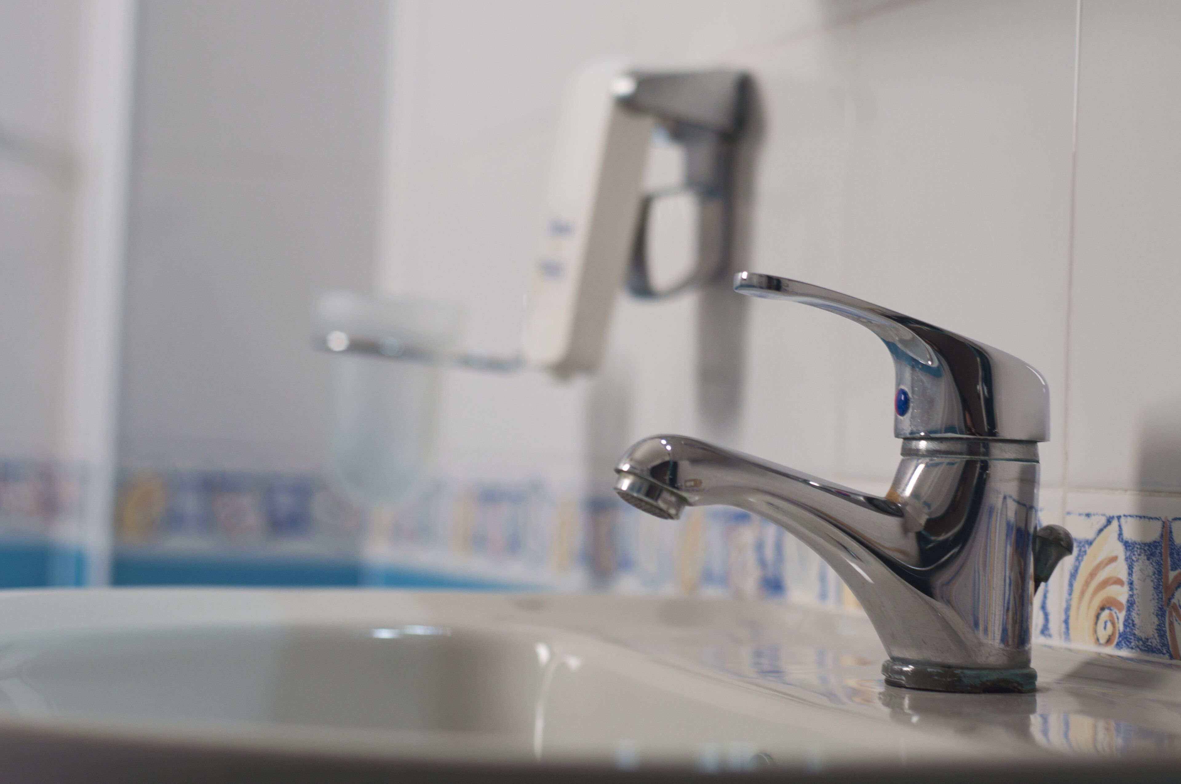 Een wastafel met een chromen kraan en een zeepdispenser bevestigd aan de muur.