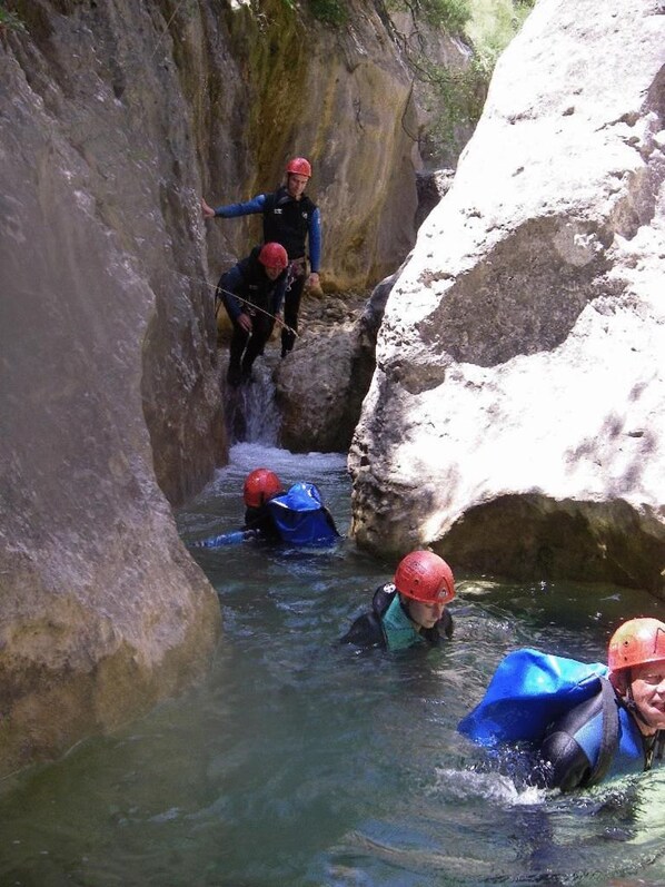 A group of people in a narrow water channel with rocky walls, wearing helmets and life jackets.