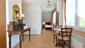 A hotel room with a wooden desk, a mirror, a bed, and a window with curtains.