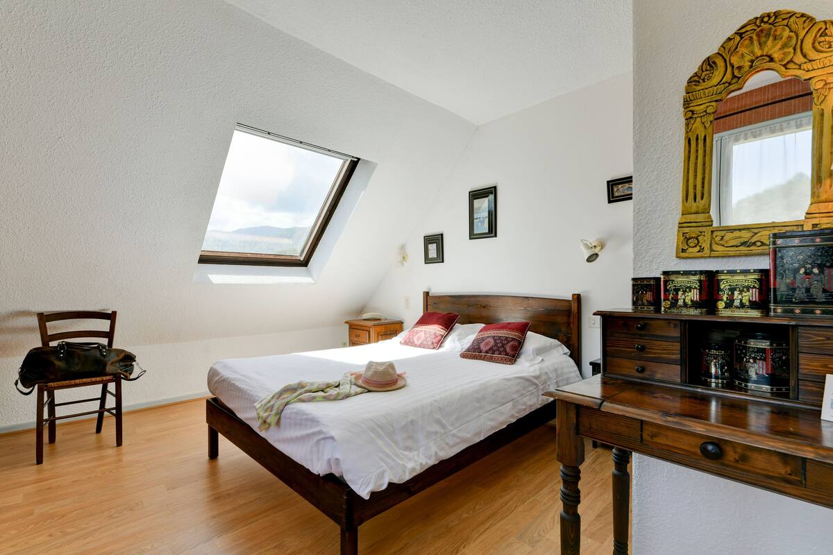 A bedroom with a wooden bed, a skylight, a wooden dresser, and a mirror with ornate detailing.