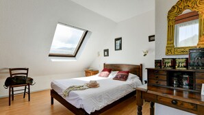 Un dormitorio con una cama de madera, un tragaluz, un aparador de madera y un espejo con detalles ornamentales.