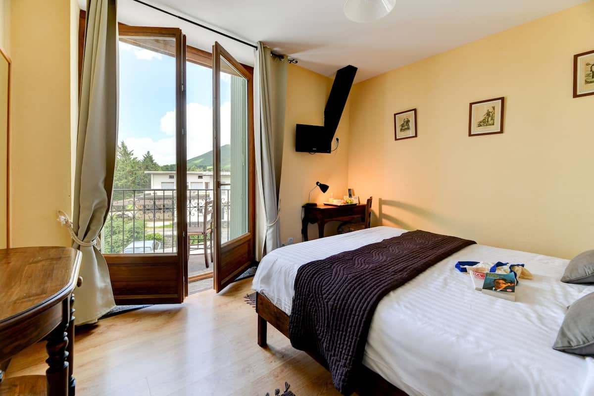 A bedroom with a bed, a desk, a chair, and a view of the outdoors through a sliding door.