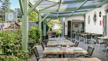 Een overdekt buitenruimte met houten tafels en stoelen, een receptiebalie en een bord dat een hotel aangeeft.