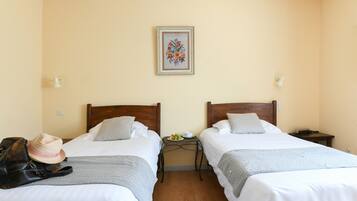 A hotel room with two beds, a nightstand with a lamp, a framed floral artwork on the wall, and a suitcase on the floor.