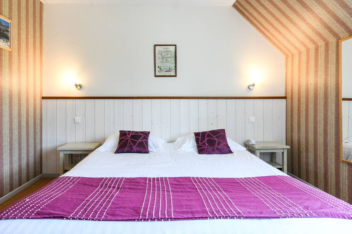 A hotel room with a bed, two nightstands, a wooden headboard, a framed picture on the wall, and a striped wall pattern.