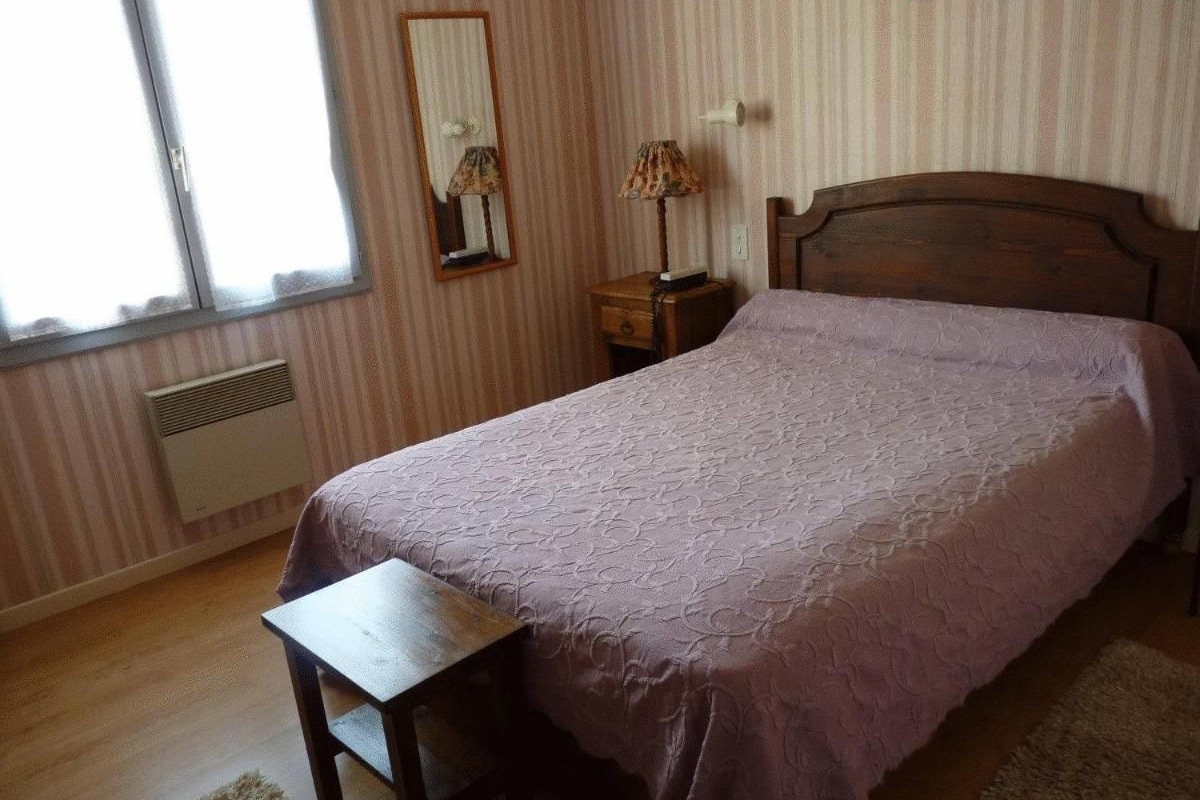 A bedroom with a bed, a nightstand, a lamp, a mirror, and a window.