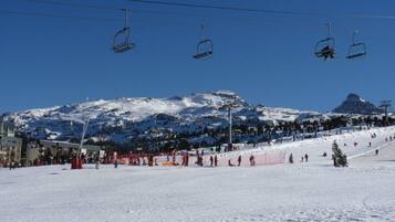 Een wintersportgebied met een stoeltjeslift, besneeuwde hellingen en een berg op de achtergrond.