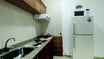 A kitchen with a granite countertop, stainless steel sink, stove, and a white refrigerator with a Samsung logo.